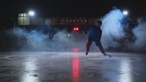 Male-hockey-player-with-a-puck-on-the-ice-arena-shows-dribbling-moving-directly-into-the-camera-and-looking-directly-into-the-camera-against-a-dark-background-in-the-smoke